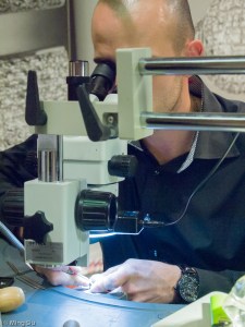 at the Gem Setter station,  artisan utilizing small hand tools and the help for microscope, mounting points are created and gems are set without glue on a bracelet.